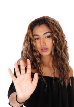 A serious looking young woman in a black top and long curly brunette .hair holding up her hand for defence, isolated for white background.