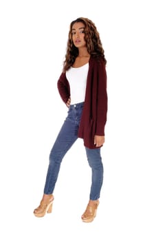 A beautiful woman with long curly brunette hair standing in jeans and a.sweater, serious looking, isolated for white background.