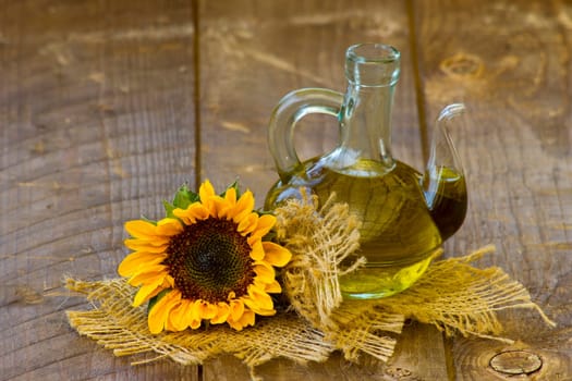 Glass bottle with sunflower oil and sunflower on wooden background