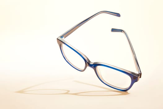 Studio shot of blue glasses with shadow at yellow background.