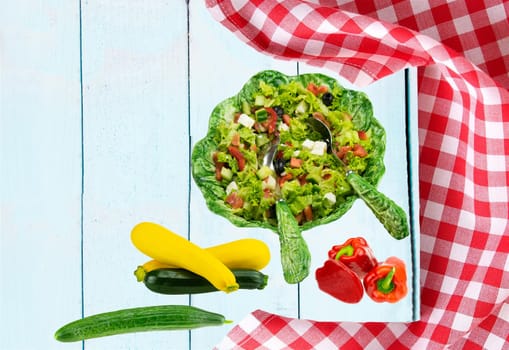 Food recipe template. Healthy fresh vegetarian vegetable spring salad in ceramic salad bowl and zucchini, cucumber and paprika on table. Health care, diet and nutrition concept.
