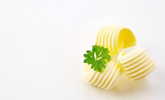 Three decorative elegant curls of farm fresh butter garnished with parsley arranged to the side on white with copy space in wide angle format