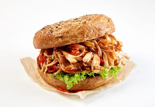Pulled chicken kebab burger on a wholegrain bun with spicy hot chili pepper and lettuce served on paper over white