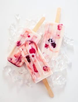 Three tasty frozen yogurt and berry popsicles for a healthy summer treat on a bed of ice made with blackberries, raspberries, strawberries and red currants