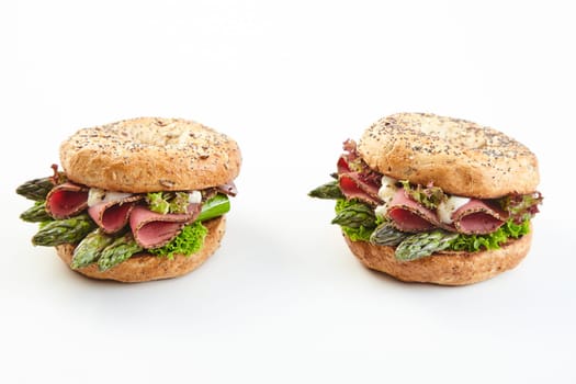Two gourmet seasonal spring asparagus burgers with fresh green spears topped with ham and mayonnaise on two buns over white with copy space
