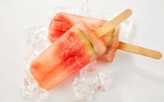 Two healthy frozen watermelon popsicles made from blended fresh fruit chilling on ice in a close up overhead view