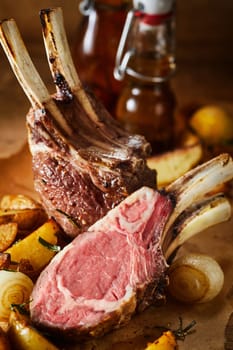 Tender barbecued rack of lamb cut through and served with roasted onions and potatoes in a close up view on the chops