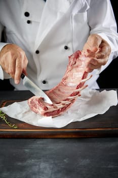 Chef preparing raw lamb chops for cooking separating the rack of lamb into portions for roasting using a knife in a close up view of his hands with copy space below