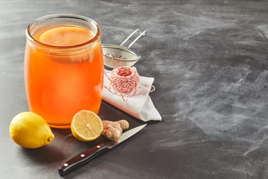 Fermented glass jar of black tea kombucha with fresh lemon and root ginger on a slate background with copy space