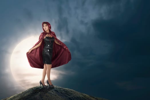 Pretty asian witch woman with red hooded cloak on the midnight