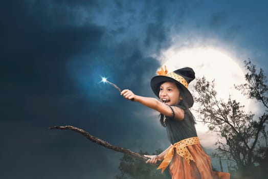 Cute asian little witch girl with magic wand on her hands over night background