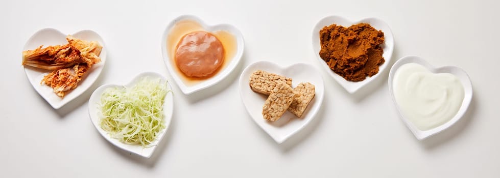 Panorama banner of healthy fermented foods arranged in a flat lay still life in heart-shaped dishes over white with a scoby fungus, pickles, vegetables and yogurt or coconut milk