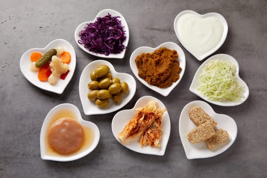 Assorted fermented foods viewed from above in heart-shaped dishes with yogurt, beet, suaerkraut, scoby, pickles, miso and olives rich in probiotics and microorganisms essential for a healthy gut