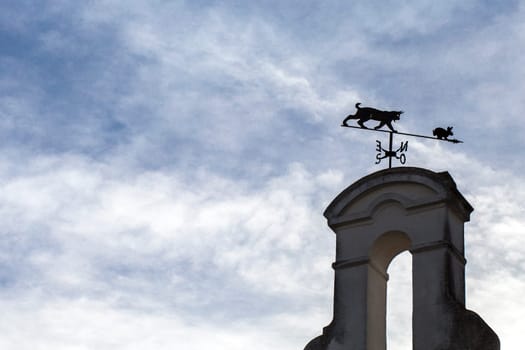 Weathercock with the shape of iberian lynx stalking a rabbit. Blue cloudy sky as background