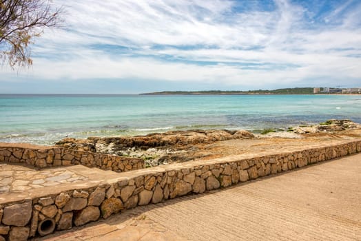 View of the turquoise Mediterranean Sea and the beach promenade in the holiday resort Cala Millor on the Spanish Balearic island Mallorca in front of a radiant blue sk