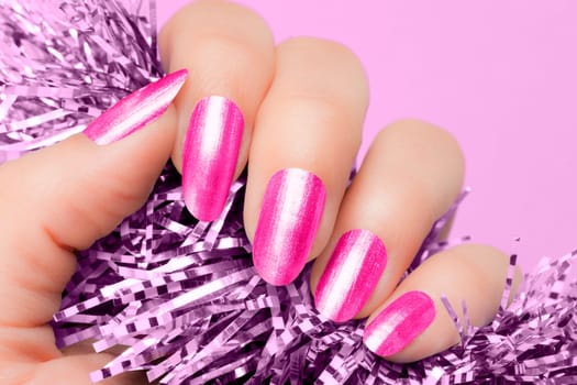 Female hand with pink nails hold purple textured decoration on purple background. Manicure concept.