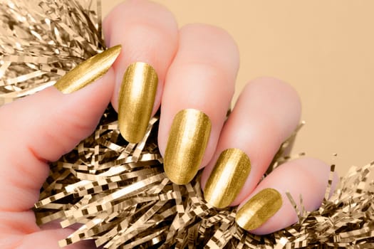 Female hand with golden nails hold beige textured decoration on beige background. Manicure concept.