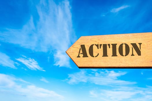 Wood arrow sign against clear blue sky with Action message