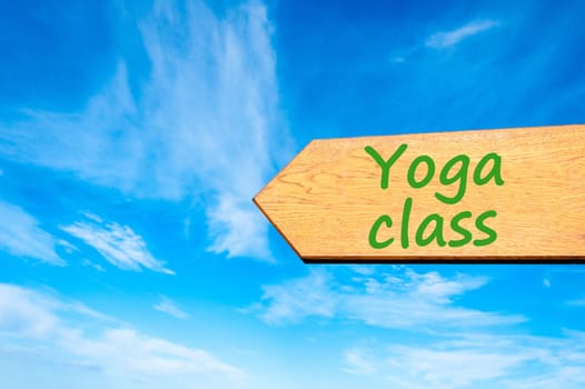 Wood arrow sign against clear blue sky with Yoga Class message