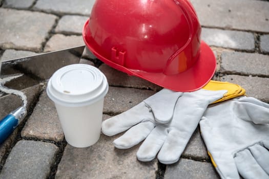 red helmet, trowel,coffee mug and work gloves on stones