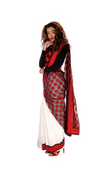 A beautiful tall woman in a colorful East Indian saree with long curly.brunette hair standing in profile, isolated for white background.
