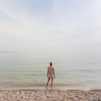 Happy Carefree Woman Enjoying Late Afternoon Walk on White Pabbled Beach in Summer.