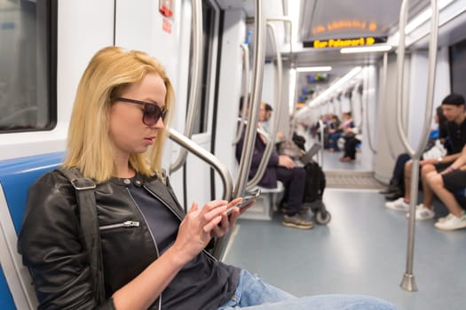 Young woman texting on mobile phone social network applications while traveling on metro. Wireless internet on public transport concept.