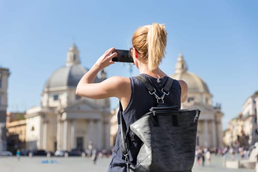 Female tourist with a fashinable vintage hipster backpack taking photo of Piazza del Popolo, People's Square, in Rome, Italy by her mobile phone.