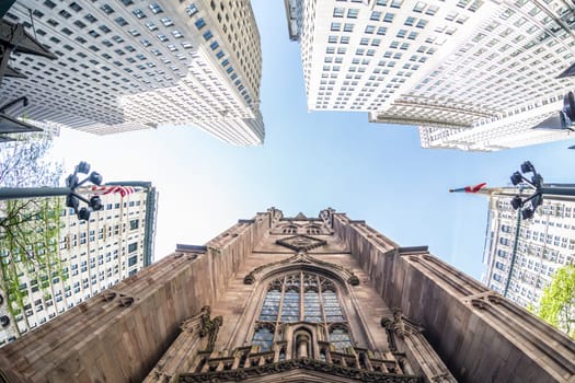 Wide angle upward view of Trinity Church at Broadway and Wall Street with surrounding skyscrapers, Lower Manhattan, New York City, USA.