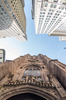 Wide angle upward view of Trinity Church at Broadway and Wall Street with surrounding skyscrapers, Lower Manhattan, New York City, USA.