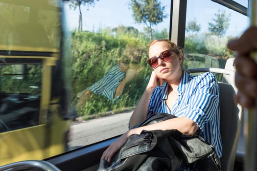 Portrait of woman sleeping on moving bus by window. Tired passenger sleeps on long countryside bus ride home.