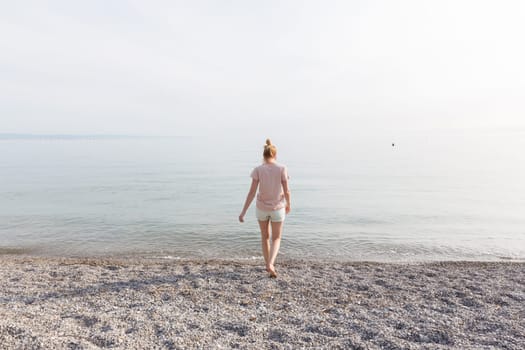 Happy Carefree Woman Enjoying Late Afternoon Walk on White Pabbled Beach in Summer.