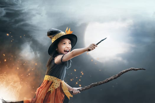 Funny asian child girl flying on the broomstick with dark sky background
