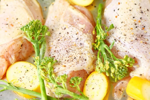 Uncooked chicken with broccolini and squash with seasoning