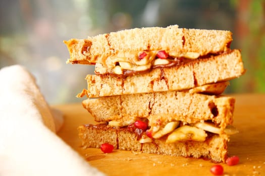 Closeup of stacked sandwich of peanut butter, chocolate spread and pomegranate seeds on cinnamon swirl bread