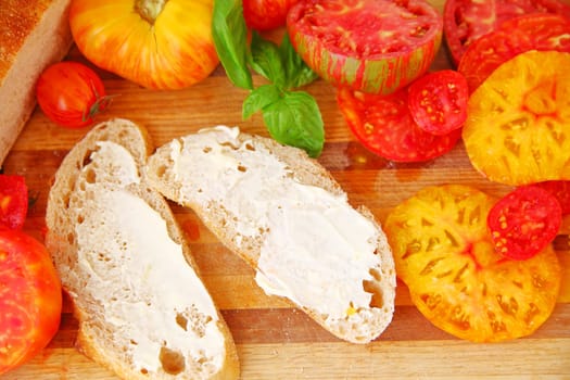 Bread slices with mayonnaise, sliced heirloom tomatoes and basil leaves on a cutting board