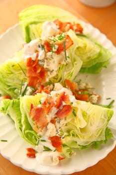 Vertical view of lettuce wedges topped with blue cheese dressing, bacon and chives