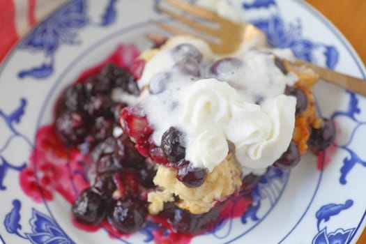 Fresh, warm cobbler with blueberries where whipped cream is melting on contact with hot fruit