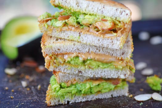 Stacked thirds of a peanut butter and mashed avocado sandwich with sliced almonds on rye toast