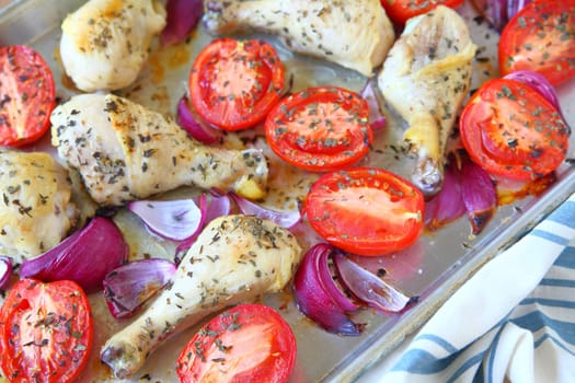 Sheet pan dinner of chicken, Roma tomatoes and red onions with dish towel
