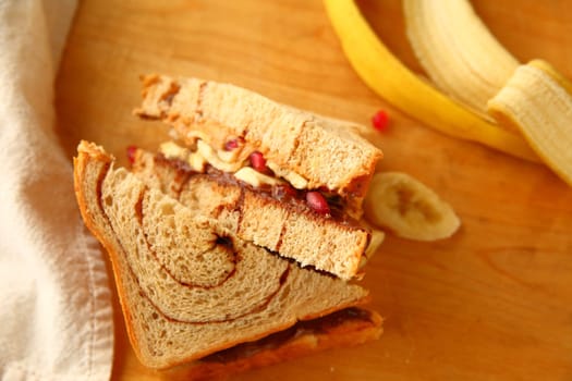 Peanut butter, hazelnut chocolate spread and pomegranate seed sandwich on cinnamon swirl bread on cutting board