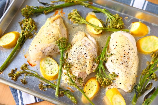 Overhead view of seasoned chicken breasts, broccolini and squash on a sheet pan.