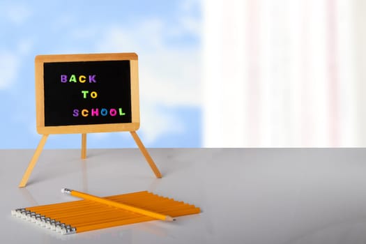 Back to school written with colorful letters on blackboard, and yellow pencils are lying on table in front of bright background. Concept education. Space for your text or display product montage.