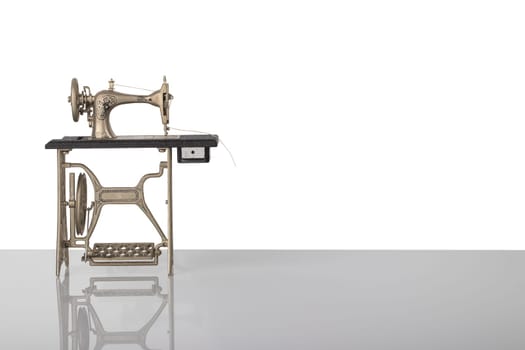 Beautiful miniature model of a vintage sewing machine on bright table isolated on white background. Advertisement for tailor business. Space for text and montage.