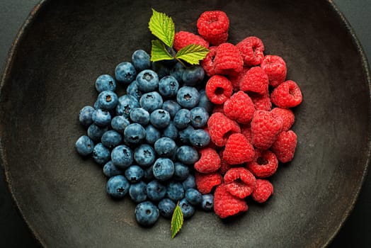 Mix of fresh berries in a bowl on black background