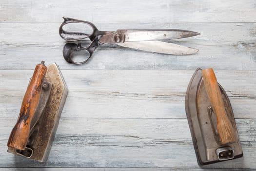 Professional old large tailor irons and one large scissors on rustic wooden table. Tailoring accessories.