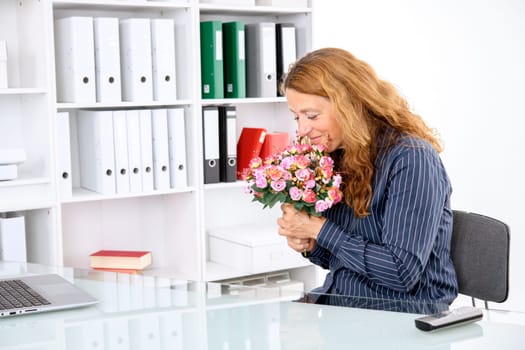 brown-haired businesswoman in the office with big bouquet of flowers