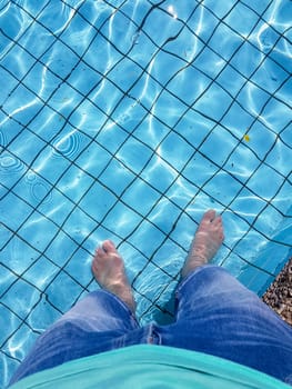Male feet with skin tanning dipping in a swimming pool