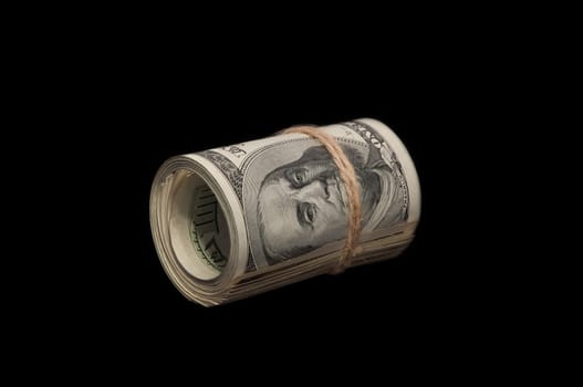 On a black background, a roll of one hundred dollar bills tied with a rope. It is located horizontally at an angle. Side view.