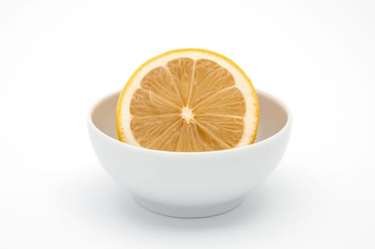 A half lemon in a white ceramics cup on a white background is isolated.